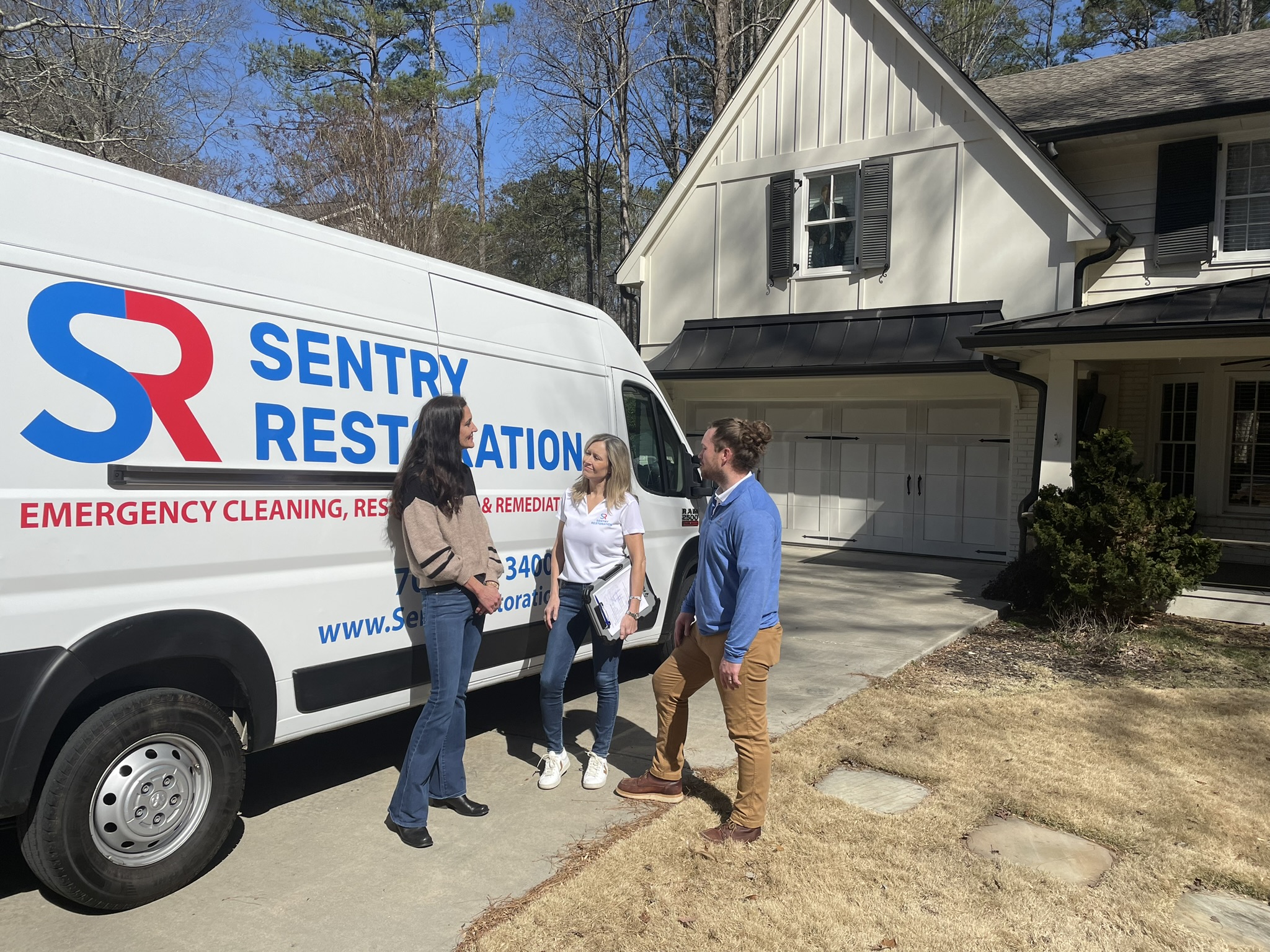 Three people converse outside a home by a Sentry Restoration service van.